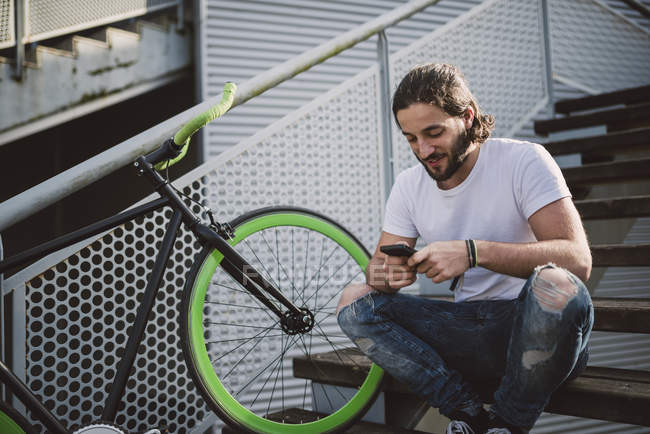 Young man sitting on stairs looking at smartphone — Stock Photo