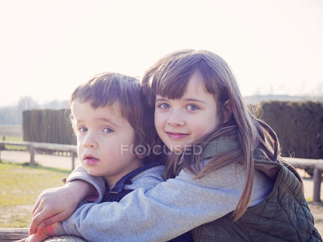 Ritratto di ragazza sorridente che abbraccia il suo fratellino — Foto stock