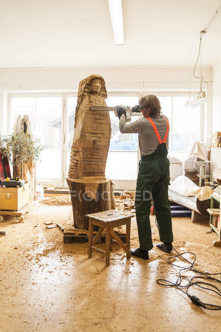 Wood carver in workshop working on sculpture with chainsaw — Stock Photo