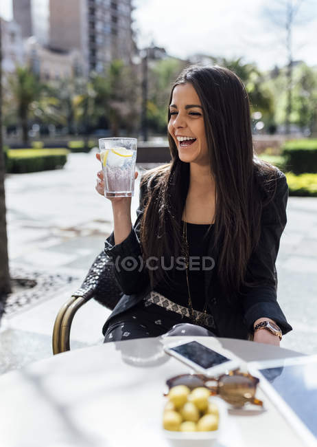 Молодий усміхається жінка сидить з напоєм на тротуарі кафе — стокове фото
