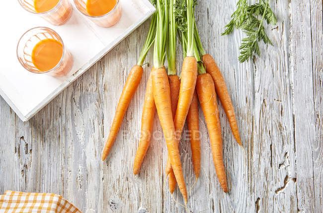 Carote e tre bicchieri di succo di carota sulla superficie di legno — Foto stock
