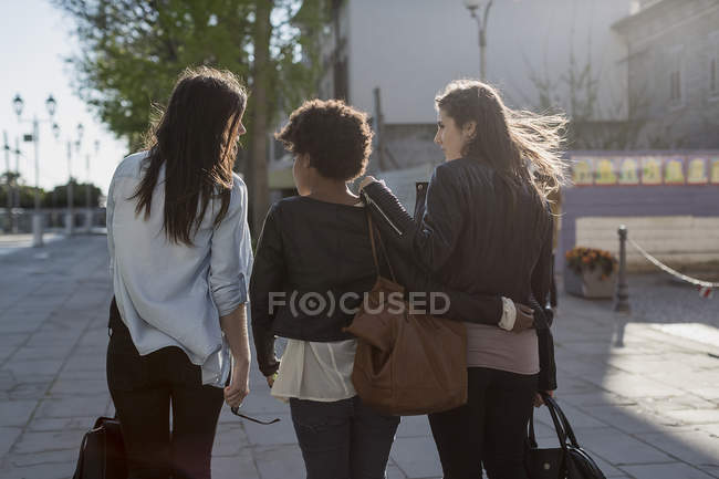 Vista trasera de tres mujeres jóvenes caminando por la ciudad - foto de stock