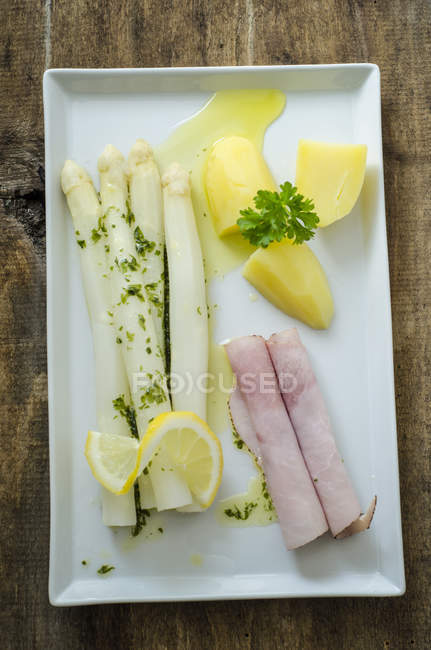 Asperges blanches au jambon cuit, pommes de terre, sauce au citron et au beurre et persil dans une assiette — Photo de stock