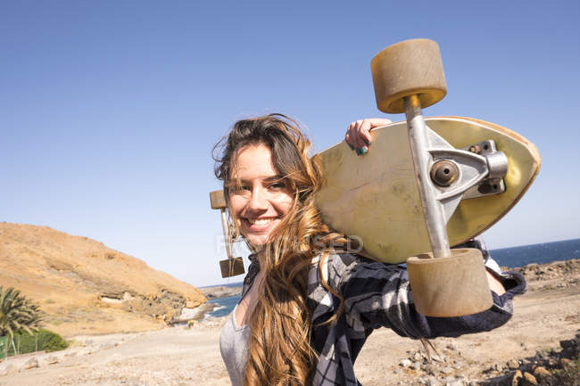 Spain, portrait of smiling teenage girl with longboard on shoulders — Stock Photo