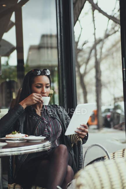 Retrato de uma jovem mulher sentada em um café olhando para tablet digital enquanto bebe café — Fotografia de Stock