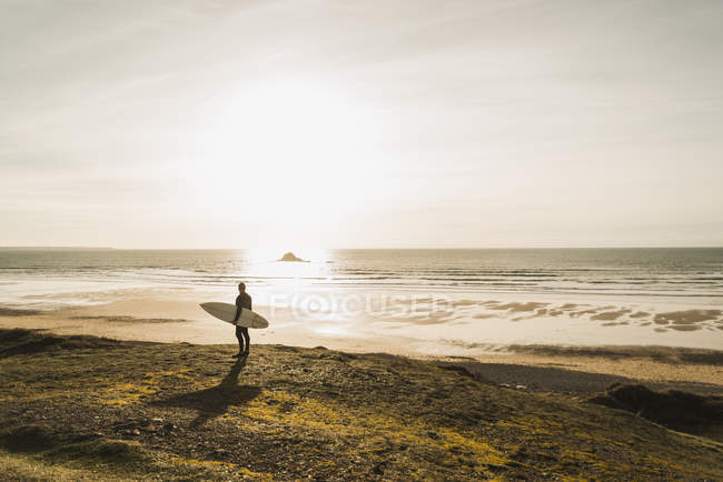 Francia, Bretagne, Finistere, Penisola di Crozon, uomo in piedi sulla costa al tramonto con tavola da surf — Foto stock