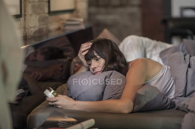 Woman lying sleepless in bed and holding alarm clock — Stock Photo