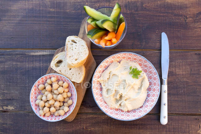 Hummus, garbanzos, zanahorias, pepino, baguette - foto de stock