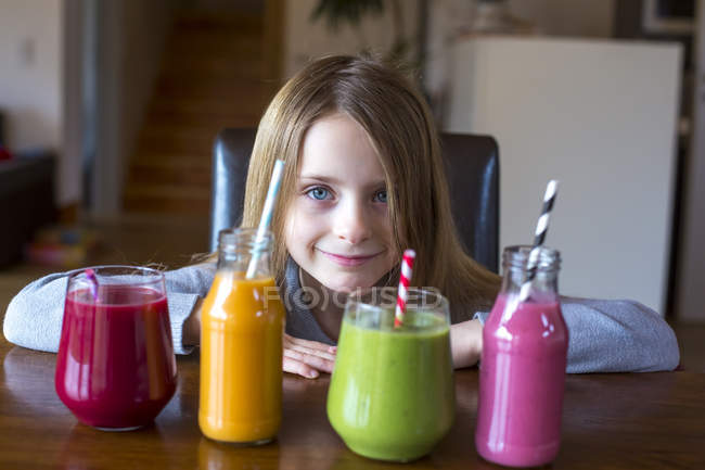 Ritratto di ragazza sorridente seduta a tavola con quattro frullati colorati — Foto stock