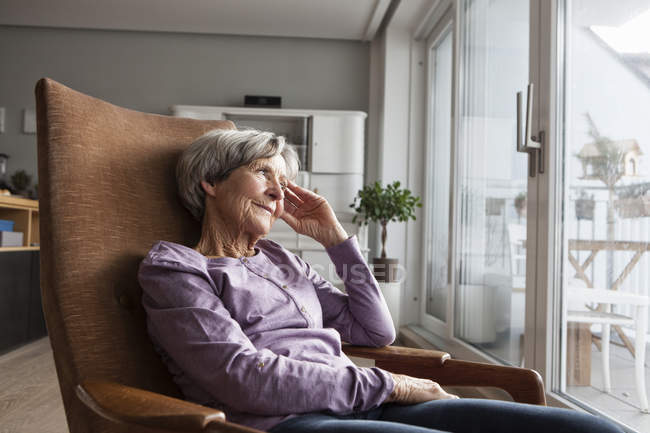 Ritratto di donna anziana seduta sulla poltrona a casa guardando attraverso la finestra — Foto stock