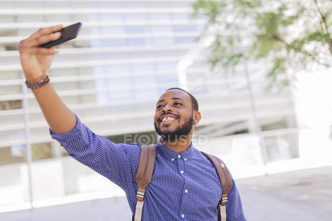 Homem africano sorridente com mochila tirando selfie com celular — Fotografia de Stock