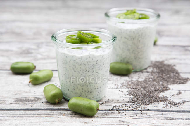 Two glasses of natural yoghurt with chia seeds and slices of kiwis on grey wood — Stock Photo