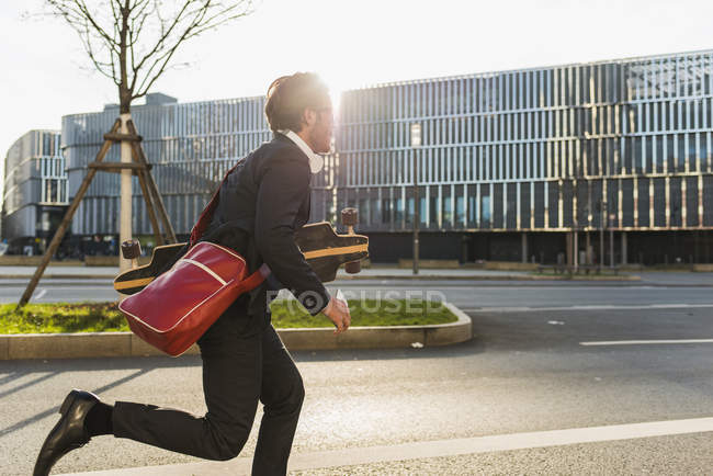 Junger Geschäftsmann läuft mit Skateboard unter dem Arm mit Handy — Stockfoto