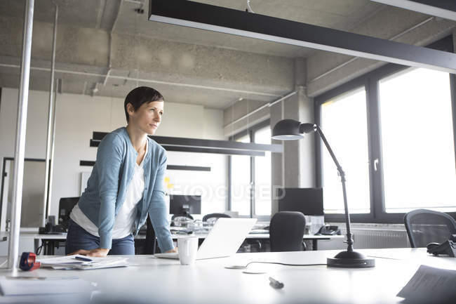 Femme d'affaires debout dans le bureau avec ordinateur portable et la pensée — Photo de stock
