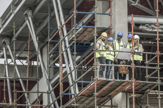 Construction workers and architects with building plan on scaffolding — Stock Photo