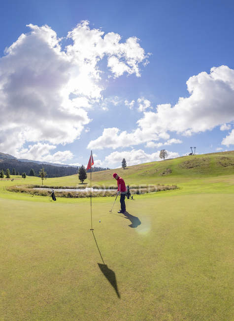 Golfista che gioca sul campo da golf, soleggiato paesaggio nuvoloso con prato erboso verde sullo sfondo — Foto stock