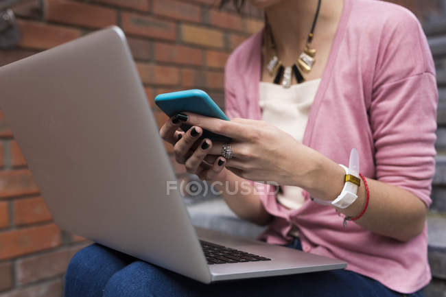 Abgeschnittenes Bild eines jungen, lässigen Mädchens mit Laptop und Handy auf Treppen — Stockfoto