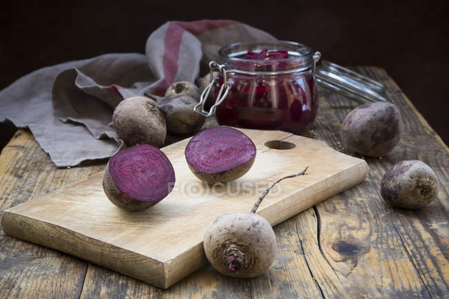 Whole and halved beetroots and preserving jar of pickled beetroots on dark wood — Stock Photo