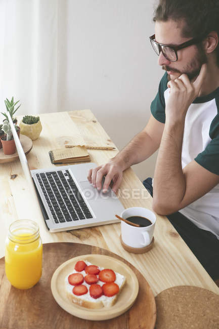 Junger Mann benutzt Laptop beim Frühstück — Stockfoto