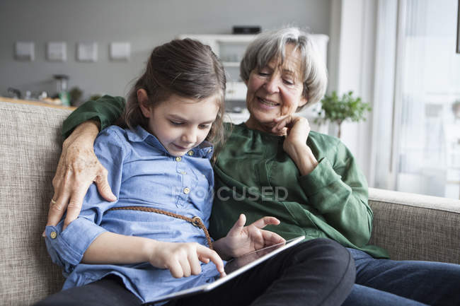 Бабушка и внучка сидят вместе на диване с цифровым планшетом — стоковое фото