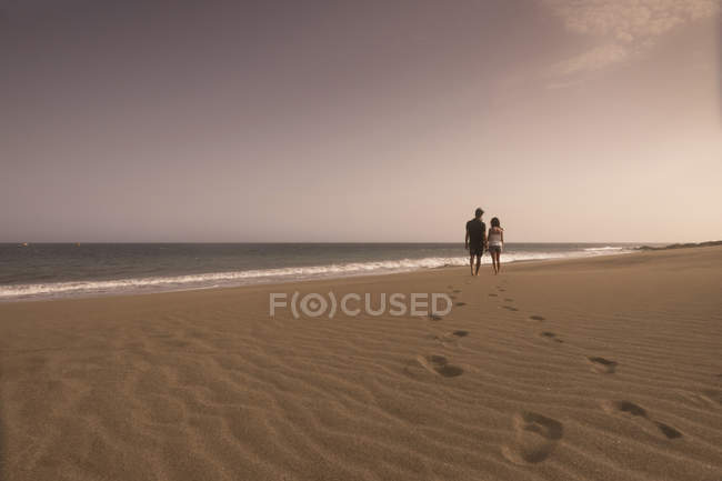 Spain, Tenerife, back view of young couple in love walking on sandy beach — Stock Photo
