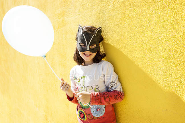 Retrato de menina rindo com balão vestindo máscara animal na frente da parede amarela — Fotografia de Stock