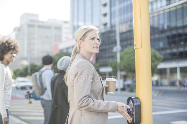 Woman waiting to cross a city street, pressing pedestrian crossing button — Stock Photo