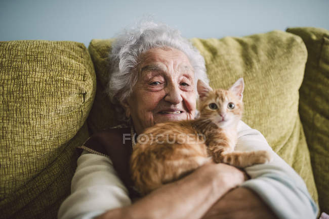 Donna anziana seduta sul divano e abbracciare gattino — Foto stock