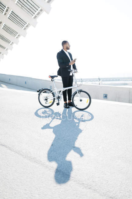 Geschäftsmann mit Fahrrad hält Handy auf Brücke — Stockfoto