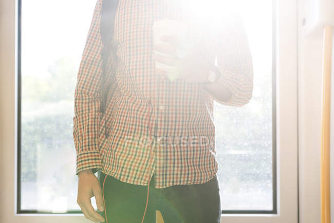 Jovem com café para ir de pé no backlight, vista parcial — Fotografia de Stock