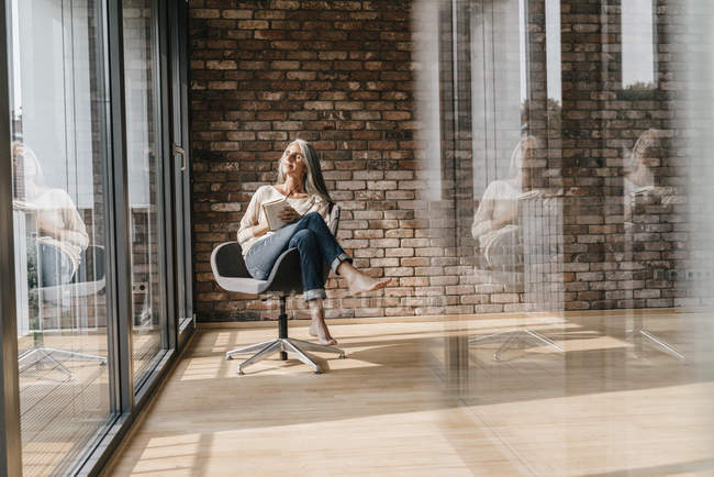 Donna con lunghi capelli grigi seduta sulla sedia alla finestra in un ufficio moderno — Foto stock