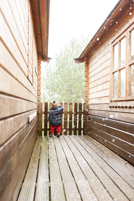 Vista trasera del niño parado entre dos cabañas de madera en invierno - foto de stock