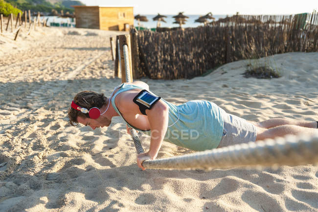 Спортсмен отжимается на веревке на пляже — стоковое фото