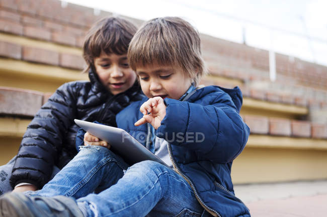 Портрет маленького хлопчика, який грає з цифровим планшетом, поки його брат дивиться — стокове фото