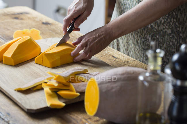 Mani femminili taglio zucca fresca sul tagliere di legno — Foto stock
