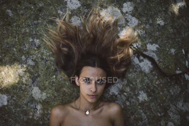 Retrato de una mujer acostada en una roca con el pelo rizado - foto de stock