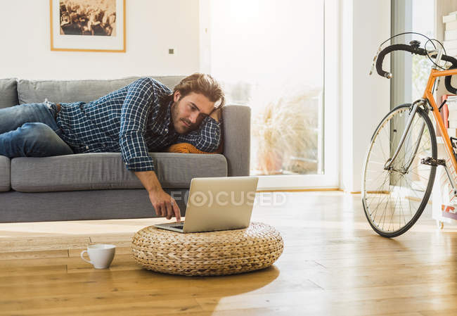 Junger Mann liegt zu Hause auf dem Sofa und benutzt Laptop — Stockfoto