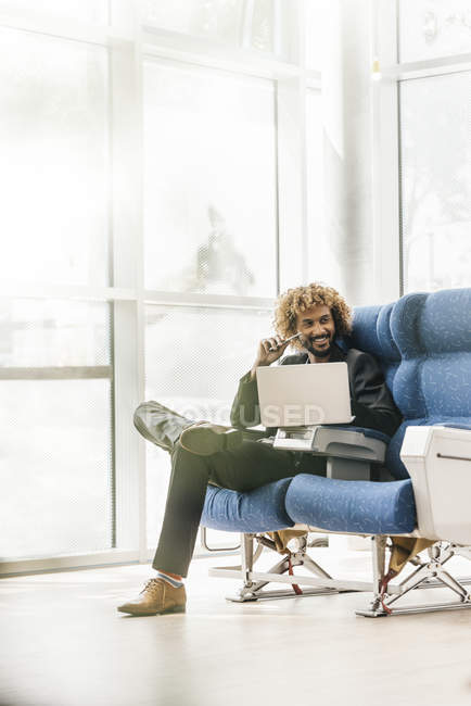 Joven hombre de negocios con éxito utilizando el ordenador portátil en sillón - foto de stock