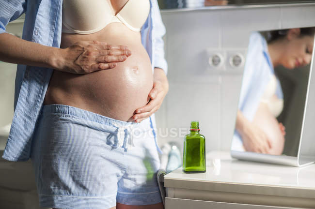 Mulher grávida no banheiro aplicando óleo na barriga — Fotografia de Stock
