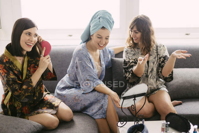 Three young women sitting on the couch wearing bathrobes preparing for the day — Stock Photo