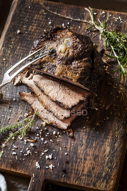 Carne asada en rodajas con romero, tomillo y sal marina sobre tabla de picar - foto de stock