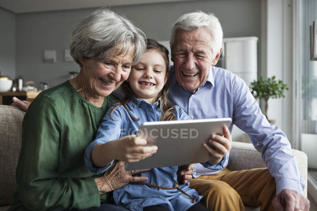 Nonni e la loro nipote seduti insieme sul divano guardando tablet digitale — Foto stock