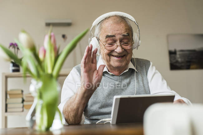 Uomo anziano utilizzando mini tablet e cuffie a casa — Foto stock
