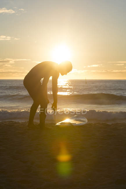 Surfer with surfboard on beach at sunrise — Stock Photo