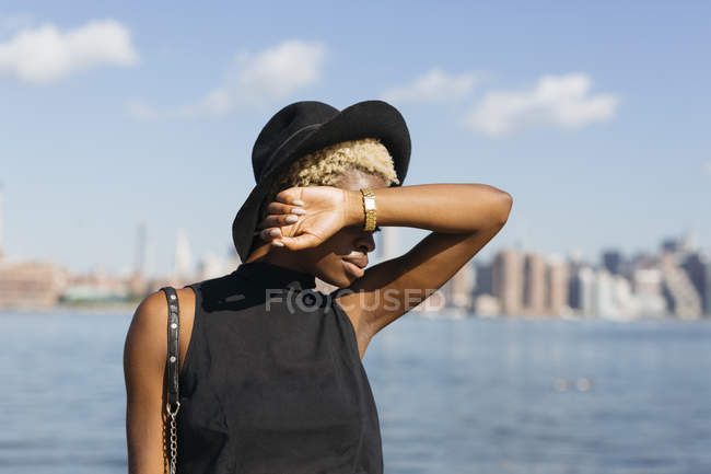USA, New York, Brooklyn, giovane donna all'East River con un cappello con gli occhi oscurati a mano — Foto stock