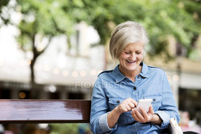 Femme adulte âgée gaie en utilisant smartphone sur fond flou — Photo de stock