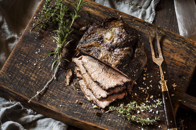 Sliced roast beef with rosemary, thyme and sea salt on chopping board — Stock Photo