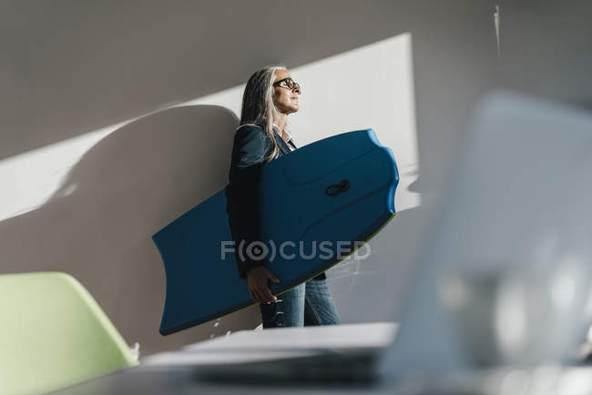 Geschäftsfrau hält Surfbrett im Büro und genießt Sonnenlicht — Stockfoto