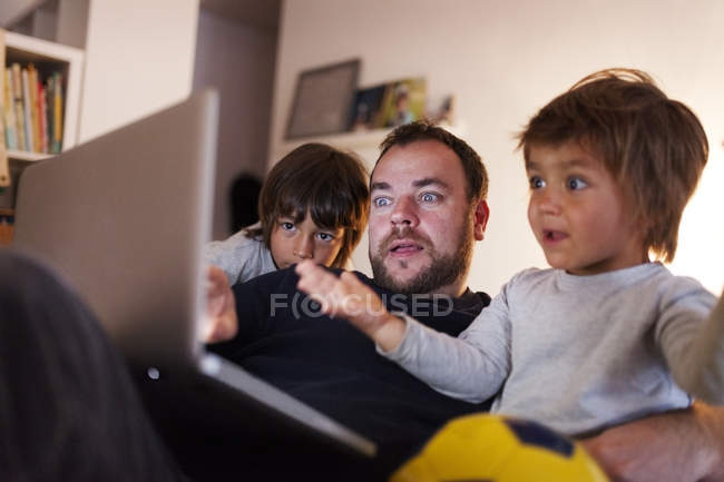 Father with two little sons watching video on the laptop at home — Stock Photo