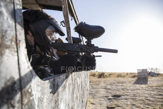 Jugador de paintball atrincherado en un autobús abandonado apuntando con pistola de paintball - foto de stock